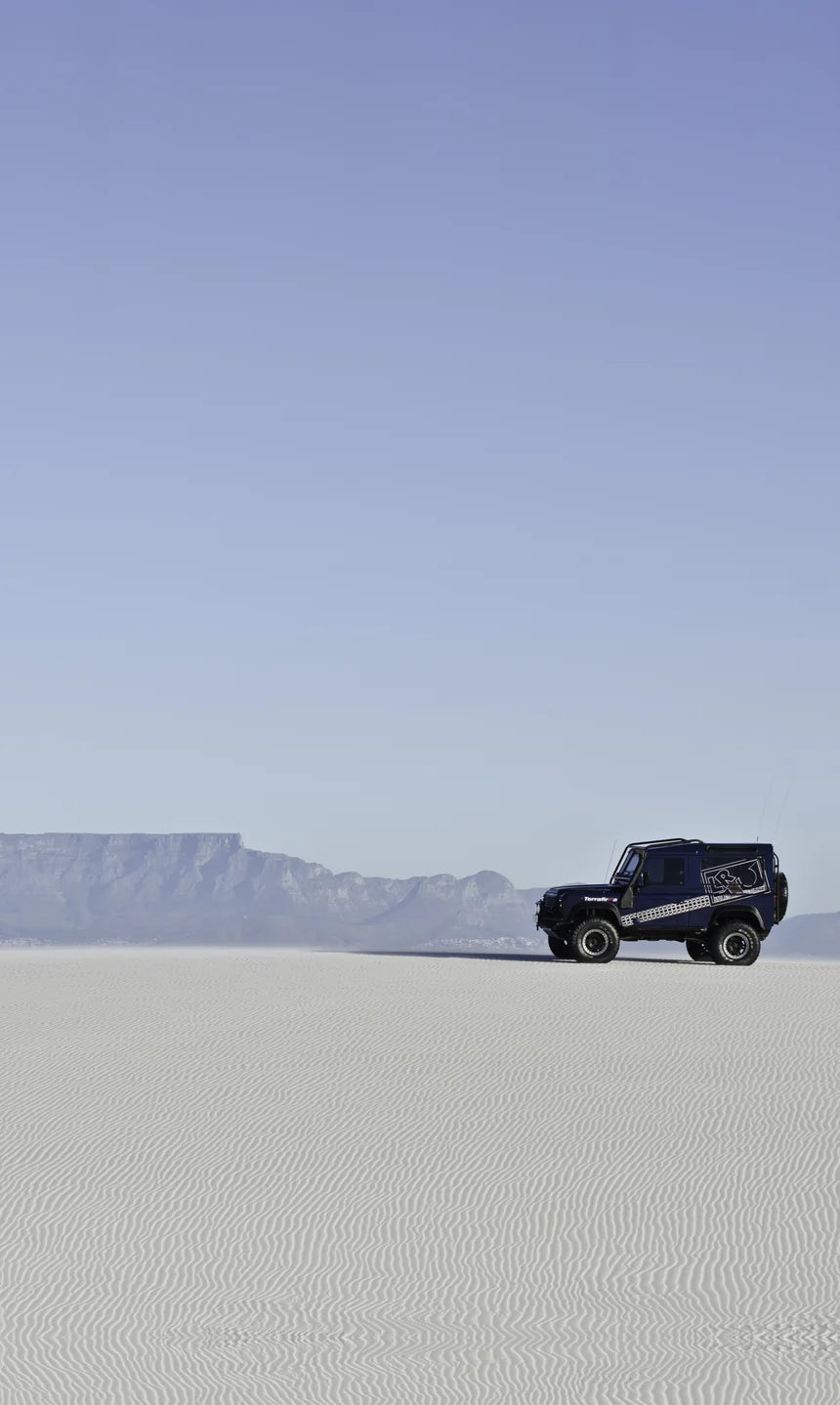Land Rover Defender on white sand dunes with Table Mountain behind